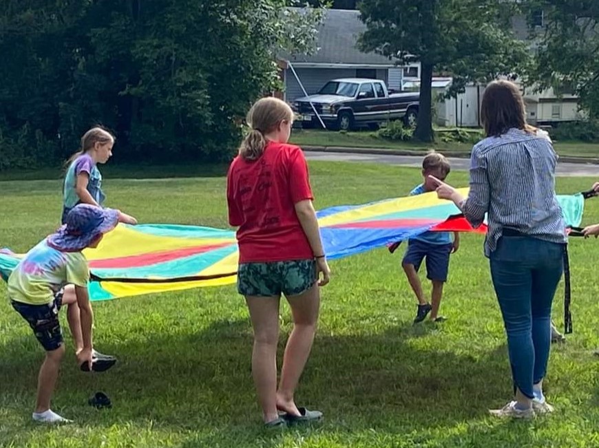 A group of youth and a librarian playing with a large multicolored parachute in the grass